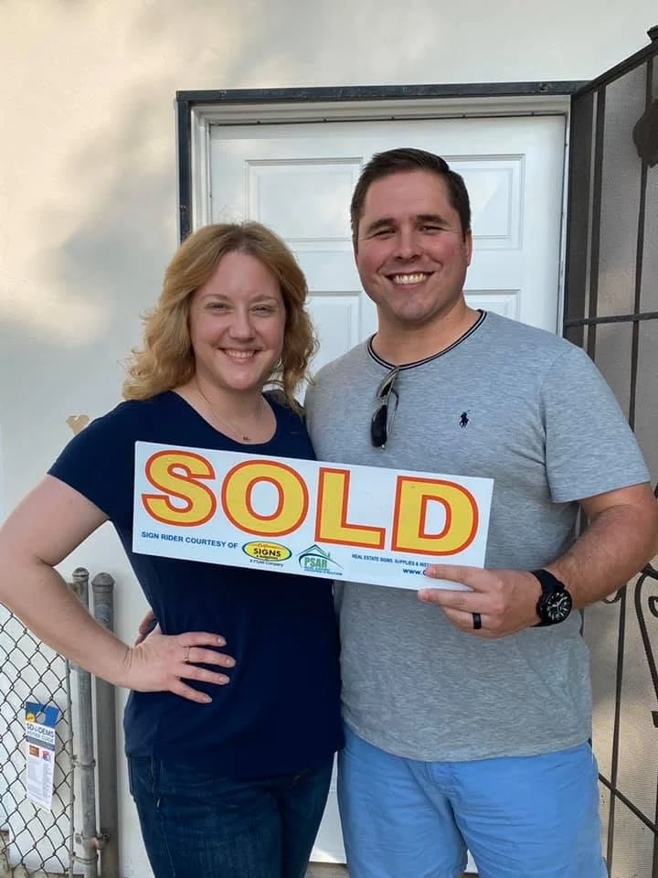 Hal and Emmy Jones holding a SOLD sign in front of the first duplex they bought