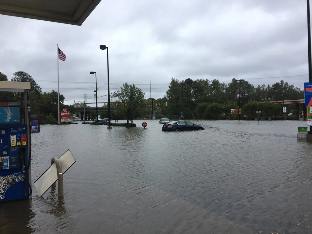 Flooded gas station and parking lot in Hampton Roads, with a car stuck in the water and an American flag